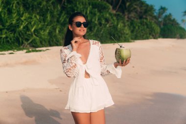 İnce parlayan tabaklanmış genç Avrupa dinlenmek için geldi, boş bir kumsalda yürür, okyanus, gülüyor ve gülümsüyor sahiptir, bir Hindistan cevizi bir saman ile tutar