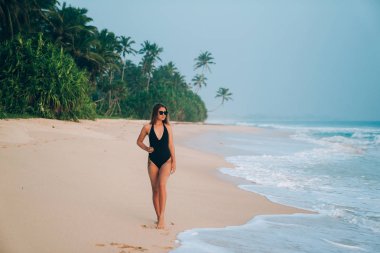 Şık bir Avrupa deniz kıyısı elini kolunu sallaya dönüyor, ince beline elini tutar, trendy güneş gözlüğü takıyor