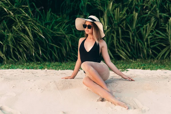 Sottile giovane bella ragazza sexy in corpo nero in posa sulla spiaggia, indossa un cappello alla moda con ala larga, godendo il suo viaggio in un paese tropicale — Foto Stock