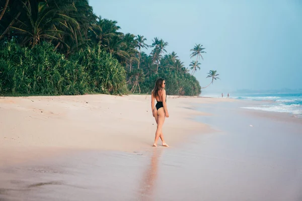 Ein schlankes junges Mädchen kam auf eine einsame Insel, schlenderte am weißen Strand entlang, bewunderte das Meer, trug einen stylischen Bikini-Badeanzug, Sonnenbrille. — Stockfoto