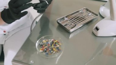 Yakın çekim yavaşladı aşağı çekim Kadın doktor tıbbi eldiven eğri cımbız yardımıyla matkap için gerekli genişliği meme dışarı alır. Diş hekimi delme önce araç hazırlar