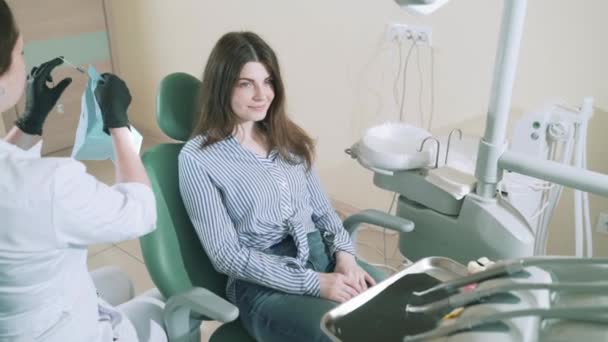 Încet, pacientul atrăgător a venit să vadă medicul dentist. Medicul își pune șorțul pe partenerul său, care stă pe un scaun — Videoclip de stoc