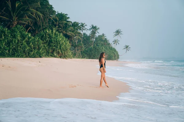 Pojetí cestování, cestovní ruch, rekreace na moři, lidi. Mladá dívka v bikinách procházky podél pobřeží růžové pláže, vlny něžně dotýkat její nohy. — Stock fotografie