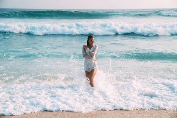 Una chica delgada y dulce con un traje de tendencia bañado en el mar, emerge de la aod, sobre el fondo de grandes olas azules altas, disfruta del sol y el descanso — Foto de Stock