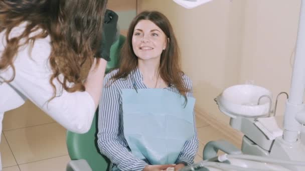 Una joven atractiva y atractiva en el consultorio de dentistas sonríe ampliamente y muestra el resultado del trabajo de los dentistas en sus dientes. 7 Limpieza y eliminación de caries, blanqueamiento de dientes. Movimiento lento . — Vídeos de Stock