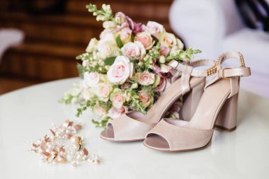 Aksesuar ve gelin kıyafetleri, yakın çekim. Bej sandalet, gelin buketi, gelinler saç süsleri, küpe.