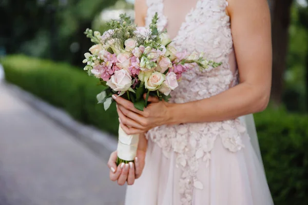 Um close-up de uma moldura de casamento cortada é um macio buquê de rosas nas mãos da noiva. Uma menina em um vestido de noiva está segurando flores . — Fotografia de Stock