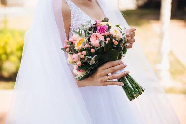 Eine Nahaufnahme einer beschnittenen Braut in einem wunderschönen weißen Brautkleid und in einem Schleier, die auf der Straße spaziert und einen Brautstrauß in leuchtenden Farben in der Hand hält. — Stockfoto