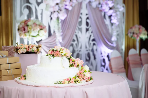 En stor vit bröllopstårta på bordet, dekorerad med färska blommor. Förberedelser för bröllop, dekorera och idé för vigseln. — Stockfoto