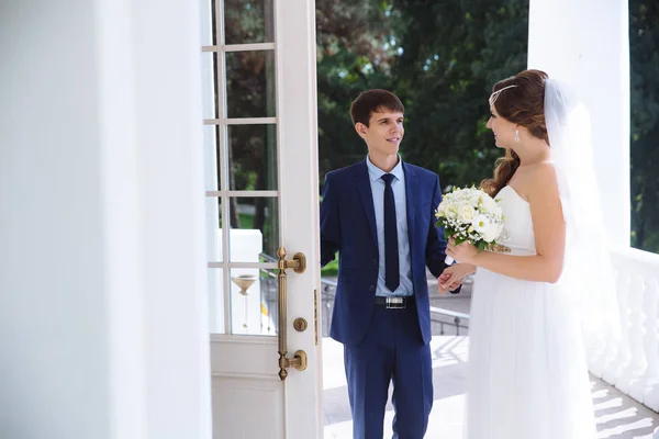 Ein Mann in einem Geschäft stilvollen Knochen öffnet vorsichtig die Tür zu einem netten Mädchen in einem Hochzeitskleid und einem Strauß Blumen. — Stockfoto