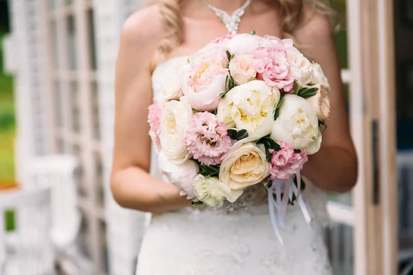 Primer plano de un marco recortado, la novia en un vestido blanco está sosteniendo su ramo de boda de peonías, mostrando flores a la cámara. Día de la boda, ramo de la novia . —  Fotos de Stock