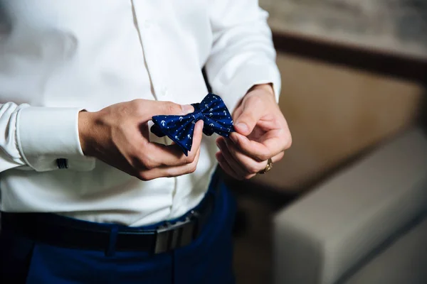 stock image A man in a business suit, a white shirt with large and dark stylish trousers, holds a blue bow tie in his hand. A businessman puts on a cufflink for his wedding, wears a gold finger ring, an expensive