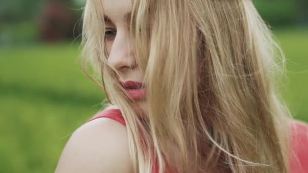 Een jong mooi meisje met een natuurlijke make-up, en losse blond haar zonder een haar is permanent buiten. Een close-up, bijgesneden vertraagd frame, model gezicht functies, het gezicht heeft betrekking op de haren die blaast — Stockvideo