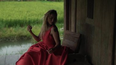 Genç iki-yıl-yaşlı yeşil bir pirinç ekili alana güzelliği onu yürüyüş evin etrafında sıcak bir gün zevk gevşek onun uzun saç düzleştirme hayran ülke evini, verandada oturuyor