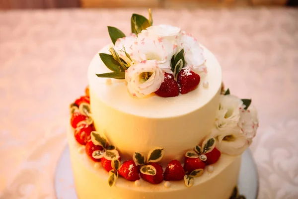 Översta närbild av en kräm tre våningar bröllopstårta. Konfektyr asteroider och dessert dekorationer för nygifta, dekorerad med jordgubbar och vita fina blommor. — Stockfoto