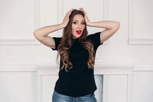 Young girl dressed in casual clothes, has long curled hair, red lips and gray eyes, is surprised by what is happening, shows an emotion of surprise, stands isolated on white background. — Stock Photo, Image