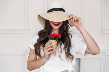 Genç güzel kadın vegan portre, büyük alanlar ile hasır şapka giyen ve gözleri, kapsayan kırmızı dudakları. Kız o kırmızı çiçekler içinde boynuz sahiptir, bu nedenle tatlılar şekil için zararlı olduğunu düşünüyor.