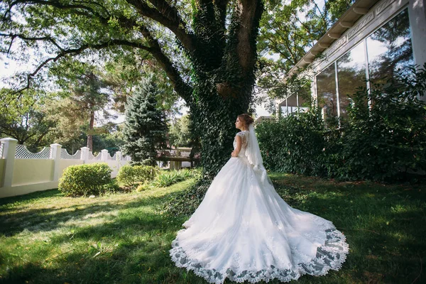 A bainha do trem do vestido de casamento branco da menina belamente encontra-se na grama verde. A noiva saiu para um passeio no jardim . — Fotografia de Stock