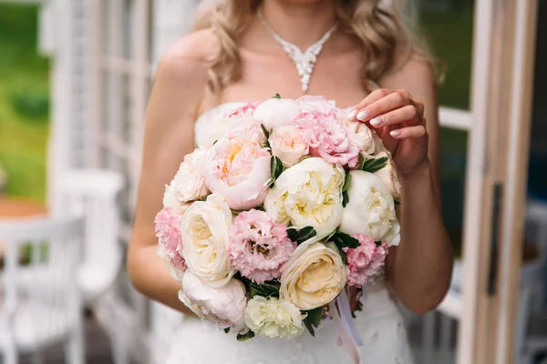 Blízký záběr oříznutého rámu, nevěsta v bílých šatech drží svou svatební kytici pivoňek a ukazuje kameře květiny. Svatební den, kytice nevěsty. — Stock fotografie