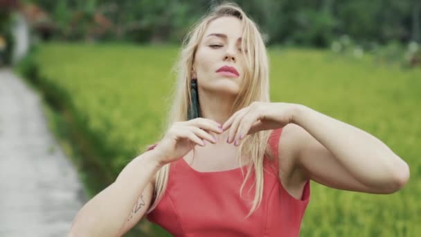 Una bella ragazza dai capelli fluenti con tatuaggi sulle mani sta ballando sul campo verde, muovendo delicatamente e sensualmente le mani lungo il viso e il corpo. Danza al rallentatore . — Video Stock