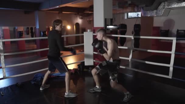 スローモーション撮影ファイト ・ クラブ。ボクサーはリングでの戦いの前に列車します。足ボクシング トレーナーと手袋で若い選手の戦闘のテクニックを実践の攻撃をかわす. — ストック動画