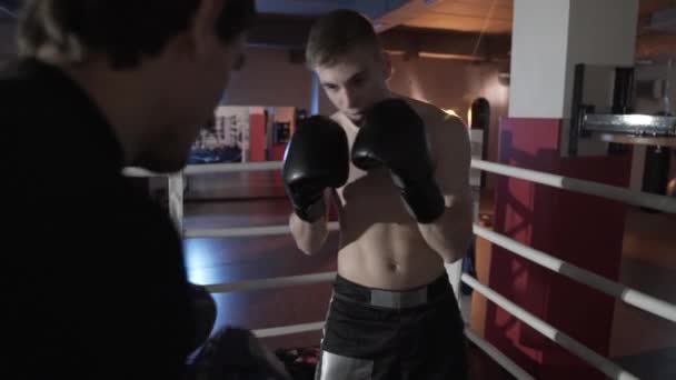 一个年轻的欧洲人的特写与一个裸露的躯干运动短裤, 穿上拳击手套列车在环与他的教练, 履行打击。运动, 男人, 拳击的概念. — 图库视频影像