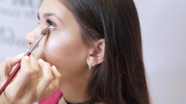 Doğal makyaj oluşturma kırpılmış çerçeve Close-up. Stilist bej gölgeler ile alt köz kapagi modellerinin boyar. Güzellik salonları, kalıcı makyaj, kadınsı görüntü, Güzellik, kozmetik kavramı.