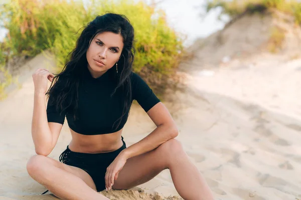 Portrait of young attractive brunette with curly hair resting on the beach, wearing an indoor black top, high trimmings on lacing and gold earrings. The girl is posing for the cover of a fashionable — Stock Photo, Image