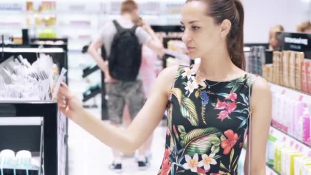 A close-up of a girl goes to the perfume and cosmetics store, chooses a make-up remover, reads labels on bottles, chooses a suitable brand. The concept of beauty, shopping. — Stock Video