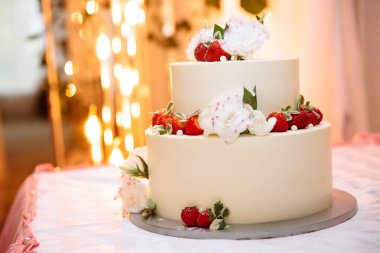 Düğün üç katlı beyaz kremalı pasta tablodur. Tatlı olgun kırmızı çilek çilek ile dekore edilmiştir ve beyaz çiçekler yaşamak. Stil düğün düğün pasta dekorasyonu için fikirler.