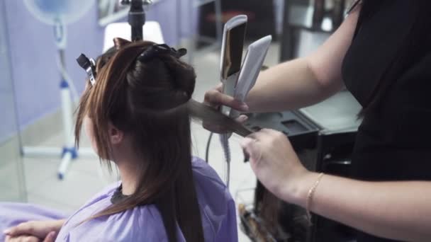 Αγορά σχέδιο αργής κίνησης γυρίσματα στυλίστας κομμωτήριο ισιώνει τα μαλλιά στους πελάτες μετά την κερατίνη ίσιωμα με ένα σίδερο κέρλινγκ, κατέχει μια χτένα μέσα από τα μαλλιά του, και στη συνέχεια με τις λαβίδες. — Αρχείο Βίντεο