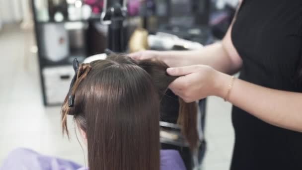 Gros plan d'une procédure de prise de vue plus courte pour le lissage des cheveux de kératine. Le coiffeur redresse les cheveux des clients avec un cheveu bouclé, sépare une mèche de cheveux et le tient avec du fer à repasser . — Video