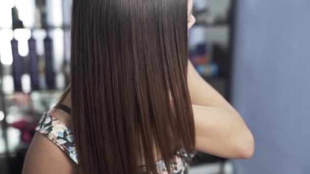A close-up slow-motion shot of a girl in a beauty salon admires her long straight shiny hair after keratin straightening. The concept of hair care in the salon, keratin, hair straightening. — A close-up slow-motion shot of a girl in a beauty salon admires her long straight shiny hair after keratin straightening. The concept of hair care in the salon, keratin, hair straightening. —