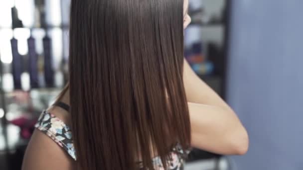 Um close-up tiro em câmera lenta de uma menina em um salão de beleza admira seu longo cabelo brilhante liso depois de endireitar queratina. O conceito de cuidado do cabelo no salão, queratina, alisamento do cabelo . — Vídeo de Stock