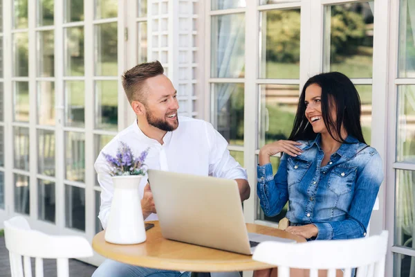 Funny people laughing while sitting at a table in a cafe. Freelancers work at the computer, have fun together. The couple in love work remotely. Concept people, technology, technology, gadgets.