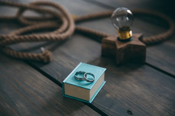 Gouden trouwringen op een blauwe geschenkdoos op een bruin houten retro tafel liggen. Decoratie met elektrische lamp, touw. Het concept van sieraden. — Stockfoto