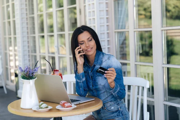 Eine schöne junge Europäerin trägt stylische Kleidung, sitzt an einem Tisch in einem Café, benutzt einen Laptop, trinkt leckere Getränke und bestellt ein Dessert, bestellt etwas in einem Online-Shop, bestätigt die Bestellung — Stockfoto