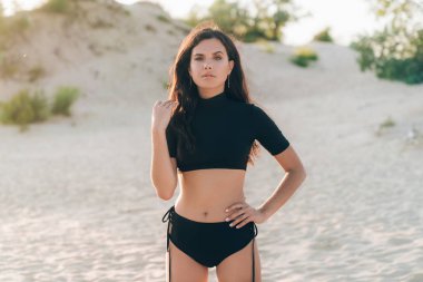 Kıvırcık saçlarını rüzgara karşı ayarlama bir mayo sahilde poz bir kıvırcık saçlı kız Close-up onun alt vurgulamak için bel üzerinde elini koydu. Boşaltmak.