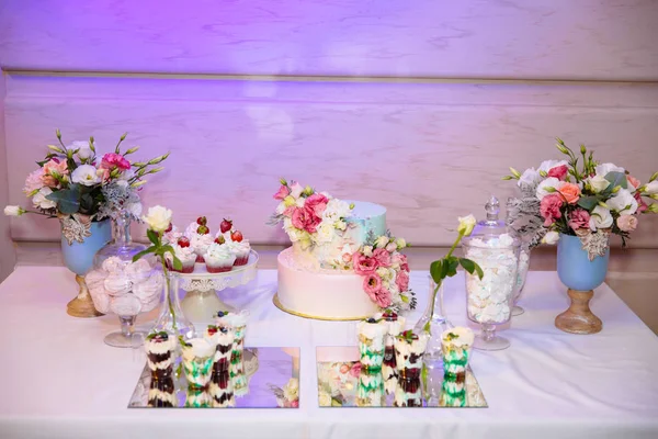 Pastel de boda multinivel y barra de caramelo, una mesa con dulces y postres en la mesa. Buffet con deliciosos cupcakes, pasteles, galletas, flores . — Foto de Stock