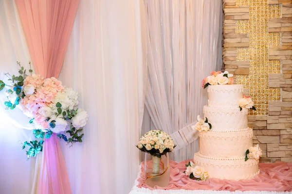 Een multi-level witte bruidstaart met bloemen versierd staat op een tafel naast een boeket van de bruid bloemen. Concept van eten, snoep en desserts op een feestje. — Stockfoto