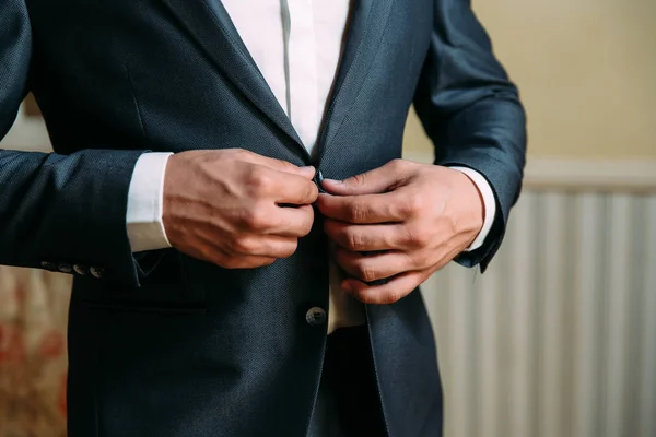 Primo piano di una cornice ritagliata di un uomo d'affari elegante abbottonarsi la giacca, in piedi in un ufficio elegante con la riparazione del progettista . — Foto Stock