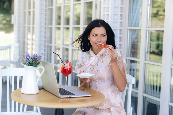 A beautiful young girl came to the pastry shop, sat down at a small table on the street, gave her laptop for work, ordered a dessert, and wanted to eat her delicious eclair. The model is not afraid to