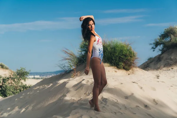 Jeune fille ludique en maillot de bain jouit de son repos sur la plage, tourbillonne et se réjouit, se réchauffe au soleil, le vent joue avec ses longs cheveux noirs . — Photo