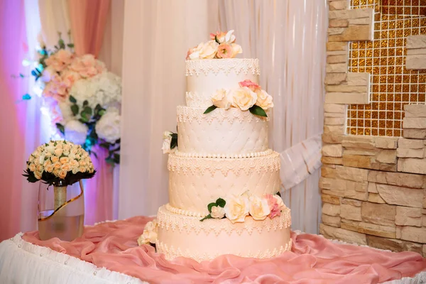 Un pastel de boda blanco de varios niveles decorado con flores se encuentra en una mesa junto a un ramo de flores de la novia. Concepto de comer, dulces y postres en una fiesta . —  Fotos de Stock