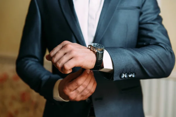 Um close-up de uma moldura cortada de um homem em um traje clássico caro olha para seu relógio. O homem de negócios está com pressa e olha para as horas. Um homem bonito com um relógio precioso e um anel de ouro . — Fotografia de Stock