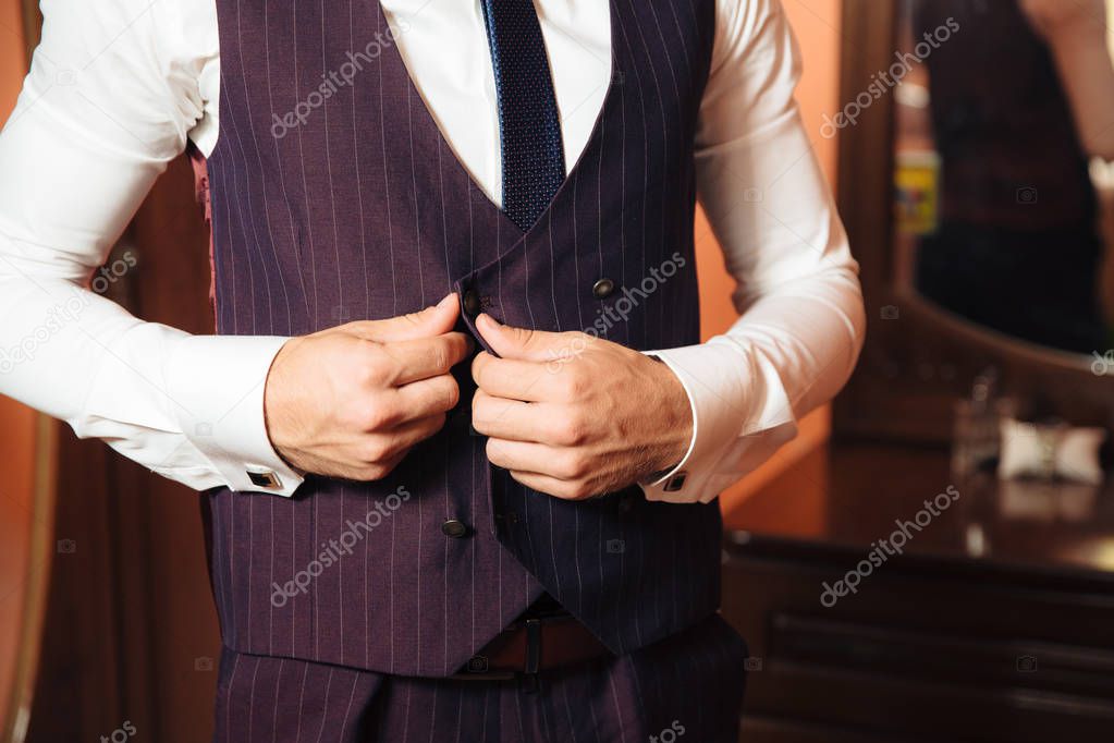Close-up of a cropped frame of a business stylish man buttoning his jacket, standing in a stylish office with designer repair.