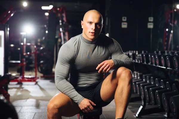 Muskulös man i en grå t-shirt vilar mellan övningar i gymmet. Atlet i gymmet — Stockfoto