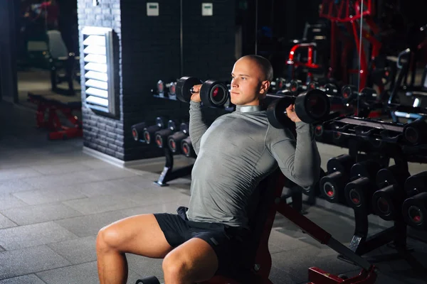 Brutala muskulös man gör sport övningar med hantlar i gymmet. En stark kille är engagerad i fitness. Begreppet idrott, hälsa — Stockfoto