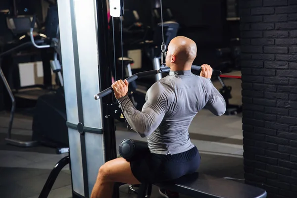 Vista trasera, hombre musculoso practicando deportes en un gimnasio. El tipo fuerte está entrenando su espalda. — Foto de Stock