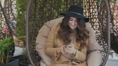 Sevimli kız sevimli çekici gülümseyerek, sallanan bir salıncak, yakın çekim, ağır çekim. O onun smartphone elinde tutuyor, siyah kıvırcık saçlı düzeltiyor.